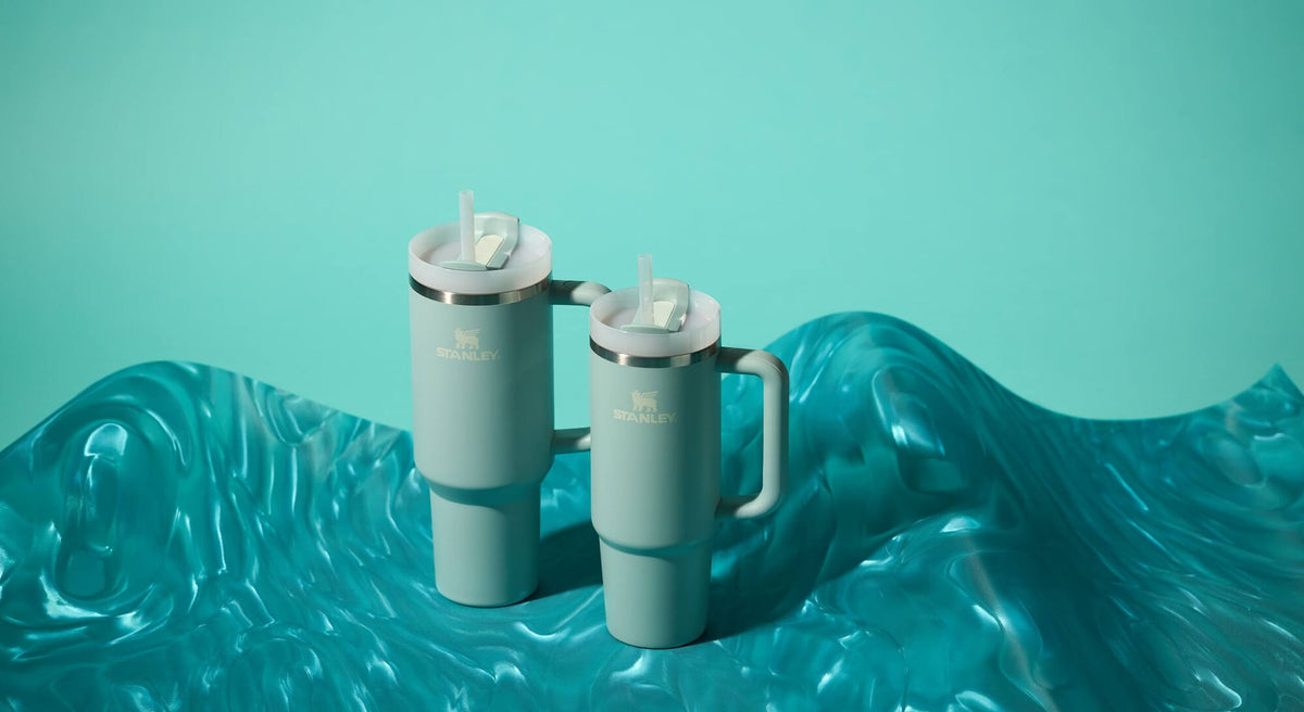 Two turquoise Quencher tumblers on a blue fabric background